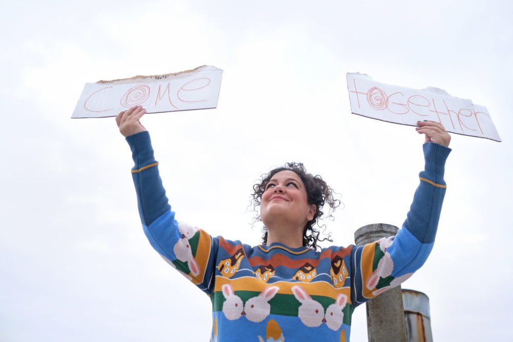 musician Tamar Haviv holds up cardboard signs that say "Come Together"