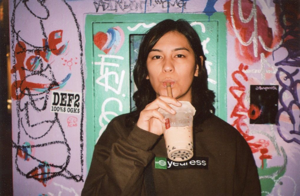 musician Zahara sips a bubble tea in front of a lavender wall covered in graffiti